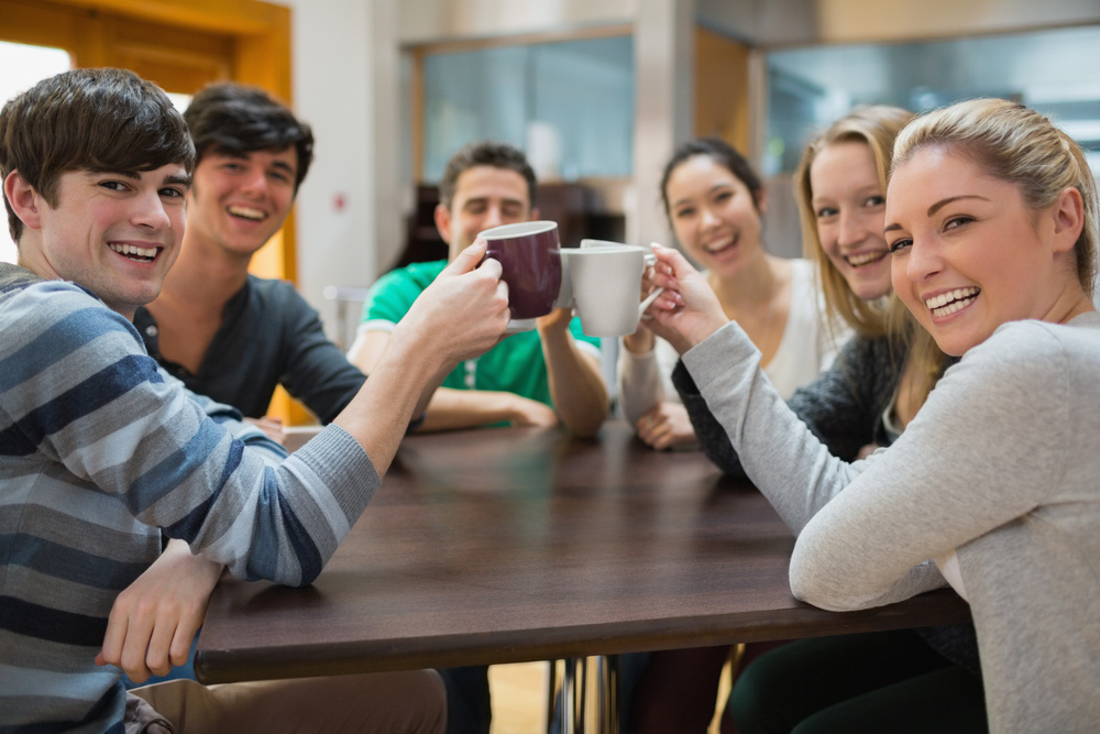 Students sitting clinking cups while smiling in college cafe